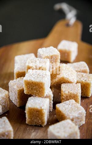 Brown cane sugar cubes on a wooden cutting board Stock Photo