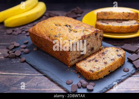 Banana bread on cutting board with chocolate chips and fresh banana in background. Stock Photo