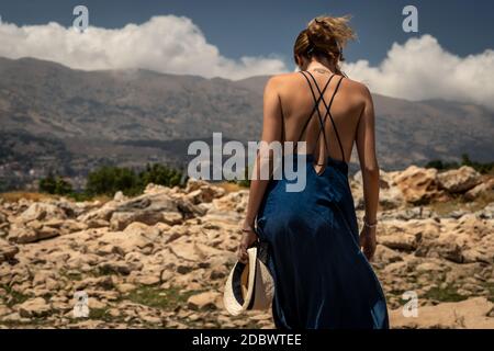 Back Side of a Beautiful Young Woman Standing on the Top of the Mountains. Enjoying Amazing Mountainous View. Happy Peaceful Summer Vacation. Stock Photo