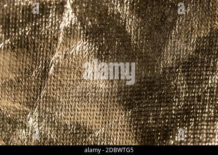 rough gold surface with sun glare as background. crumpled texture of smooth material patterned uneven. selective focus Stock Photo
