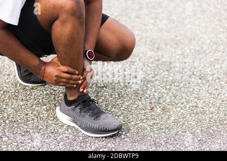 Close up Asian young sport runner black man wear watch hands joint hold leg pain because of twisted ankle broken while running at the outdoor street h Stock Photo