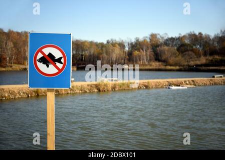 Prohibitory sign fishing is prohibited on background of two lakes and autumn forest in the park. Stock Photo