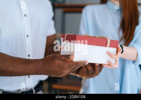 Close-up view of woman giving gift box to colleague at office.  Stock Photo