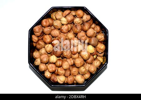 Black octagonal bowl full of peeled hazelnuts isolated on white background Stock Photo