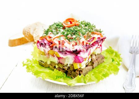 Puff salad with beef, potatoes and beets, pears, Korean spicy carrots, seasoned with mayonnaise and garnished with dill on a green lettuce in a plate, Stock Photo
