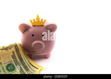 Pink piggy bank with golden crown and stack of US dollars in front isolated over white background with copy space, cash is king concept image