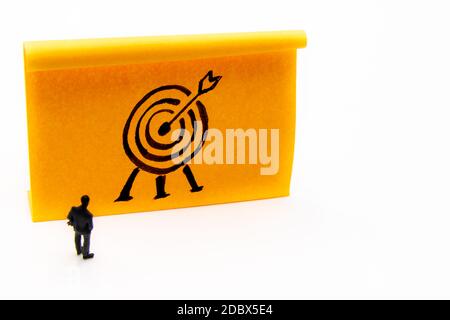 Miniature figurine posed as businessman in front of target hand drawn on adhesive paper note, performance concept image