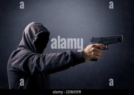 Hooded man with a gun in the dark Stock Photo