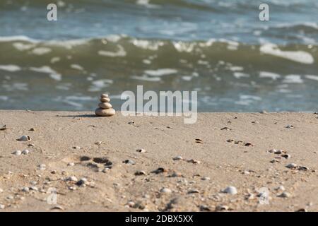 Pyramid is made of white stones against the background of sea waves. Pebble stack on the seashore Stock Photo