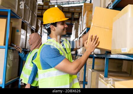 Indian warehouse worker put cardboard box in to shelf with muslim Islam asian worker do inventory in warehouse distribution center environment. Using Stock Photo