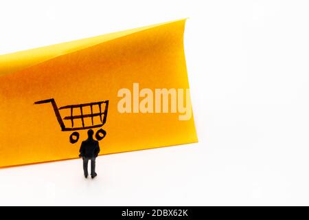 Miniature figurine posed as businessman looking at shopping cart handrawn on adhesive paper note, e-commerce concept image Stock Photo