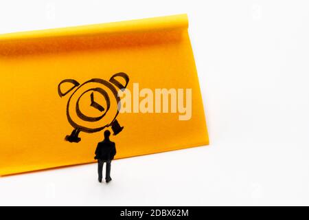 Miniature figurine posed as businessman in front of handrawn clock on adhesive paper note, time management concept image