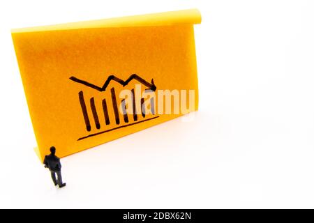 Miniature figurine posed as businessman in front of descending graph arrow hand drawn on adhesive paper note, negative performance concept image