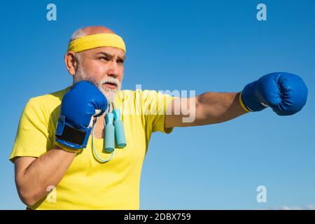 Senior sportive man in boxing stance doing exercises with boxing gloves. Elderly man hitting punching bag. Senior men fighting poses. I love boxing. Stock Photo