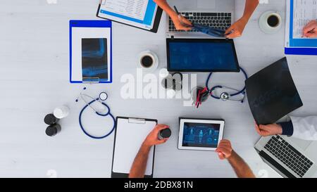 Group of doctors working together, taking notes and analysing x-ray on top view copy space sitting on desk with stethoscope and digital device all around having medical conference. Stock Photo