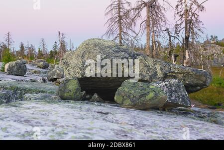 Massive megalithic stone boulders and dry dead trees in the nature reserve of mount Vottovaara. Mystical seids under a pink northern sky during the wh Stock Photo
