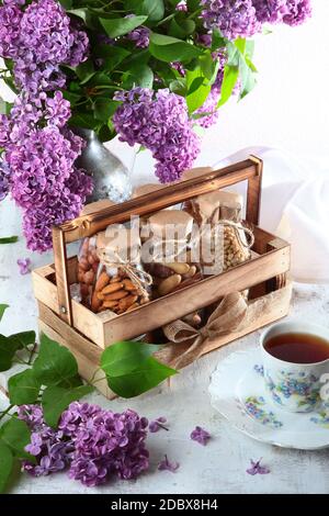 Wooden box with glass bottles with nuts. Organic food. Bouquet of lilac on the table.Vertical photo on a white background. The concept of still life. Stock Photo