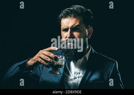 Bearded and glass of whiskey. Man Bartender with beard holds glass brandy. Alcohol concept. Stylish elegant bearded man Bartender holds whiskey glass. Stock Photo
