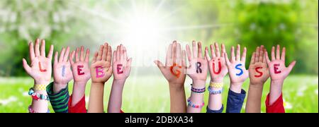 Children Hands Building Colorful German Word Liebe Gruesse Means Best Wishes. Sunny Green Grass Meadow As Background Stock Photo