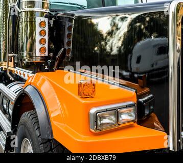 Front part of commercial freight transportation stylish black and orange big rig semi truck tractor with chrome accessories and glass headlight and re Stock Photo