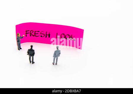 Presentation meeting with miniature figurines posed as business people standing in front of post-it note with Fresh Look handwritten message in backgr Stock Photo