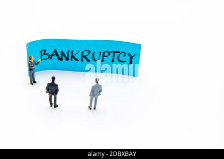 Presentation meeting with miniature figurines posed as business people standing in front of post-it note with Bankruptcy handwritten message in backgr Stock Photo