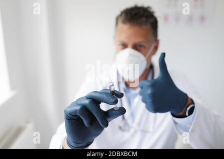 Doctor with nose and mouth mask holds syringe with the remedy against covid 19 Stock Photo
