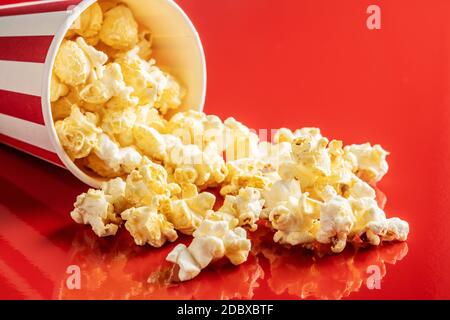 Sweet popcorn in striped paper cup on red background. Stock Photo