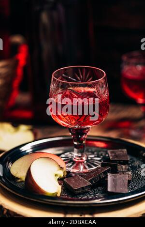 Glass of homemade redcurrant nalivka with apple slices and chocolate on metal plate Stock Photo