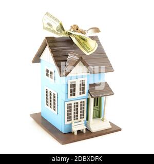 A conceptual image with a small bird holding a hundred dollar bill in its beak while resting on top of a miniature house. Stock Photo