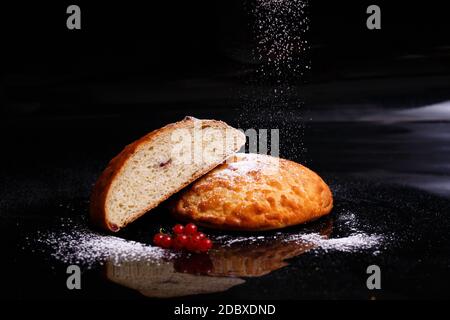 Sweet cupcake in round bread shape with filling. Bread - cupcake on a black background, sprinkled with powder, decorated with currants. Photo in secti Stock Photo
