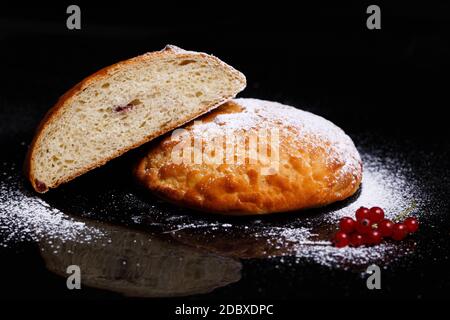 Sweet cupcake in round bread shape with filling. Bread - cupcake on a black background, sprinkled with powder, decorated with currants. Photo in secti Stock Photo