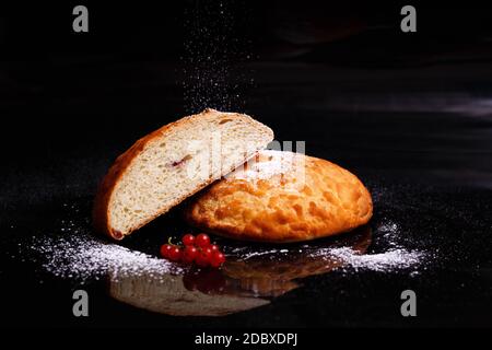 Sweet cupcake in round bread shape with filling. Bread - cupcake on a black background, sprinkled with powder, decorated with currants. Photo in secti Stock Photo