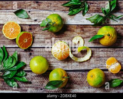 Green mandarines on old wooden background. Fresh ripe half, whole and peeled green tangerines with leaves, top view or flat lay Stock Photo