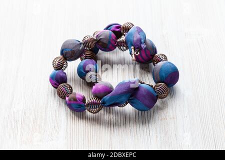 tangled handcrafted necklace of round beads wrapped in blue silk cloth and metal spiral beads on wooden table Stock Photo