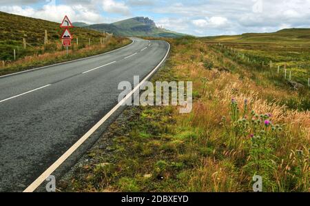 Wide shot of empty road, curve, bumps and reduce speed now sign with Old Man of Storr mountain in the background. Isle of Skye, Scotland, United Kingd Stock Photo