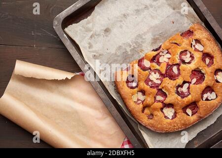 baked sponge cake with plums in a metal baking sheet on a brown wooden background, top view Stock Photo