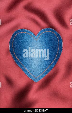 Heart of denim fabric with yellow stitching on red silk, with space for your text Stock Photo