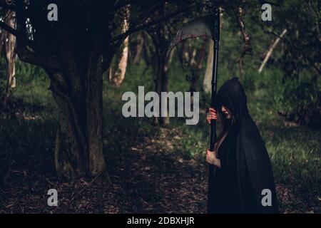 Woman horror ghost holding reaper in forest, halloween concept Stock Photo