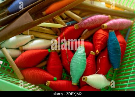 Top view colorful yarns on spool and empty wooden spools in plastic basket. Yarns in weaving shuttle tool. Textile fabric weave tools. Equipment for t Stock Photo