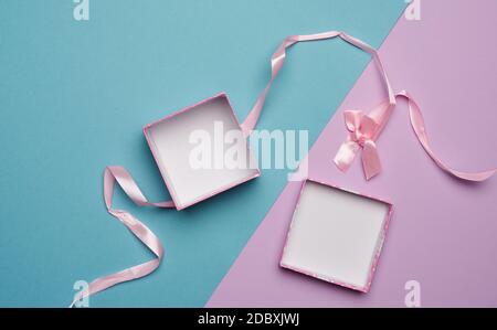 empty open cardboard box and pink ribbon with bow on blue lilac background, flat lay Stock Photo