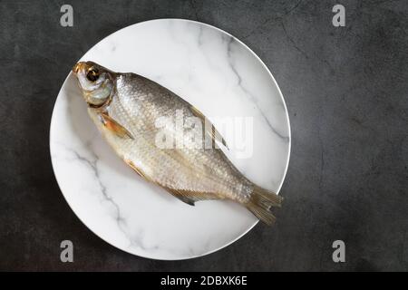 On the plate is salted and dried fish. Presented on a dark background. The view from the top, flat position, copy space Stock Photo