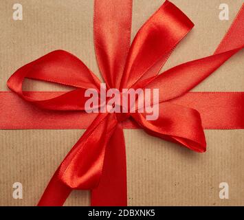 knotted bow made of red silk ribbon on brown kraft paper background, festive backdrop Stock Photo