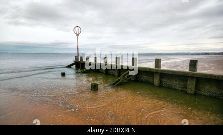 Old wooden groyne structure covered with green algae on Portobello beach during low tide with North sea in the background shot on overcast day. Edinbu Stock Photo