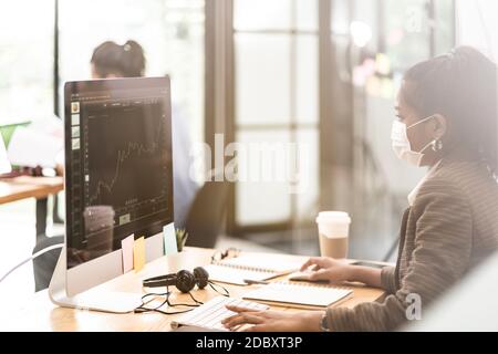 Mixed race of African black and asian businesswoman office worker wear protective face mask working in new normal office with social distance between Stock Photo