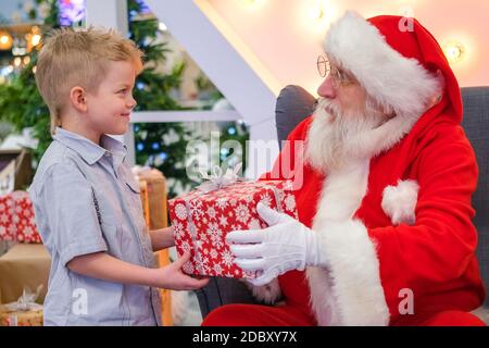 Santa Claus gives boy a gift in Shopping Mall. Real authentic Santa talking and playing surprise games with kids . Christmas sales and wishes Stock Photo