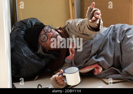 The depressed homeless man gets money help from passer-byes. he is unemployed and jobless due to the Coronavirus 19 pandemic. He lives by the sidewalk. Stock Photo