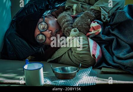 The tiring homeless man takes a nap by the sidewalk as he asks for help from passer-byes. He is jobless and depends on people's charity. Stock Photo