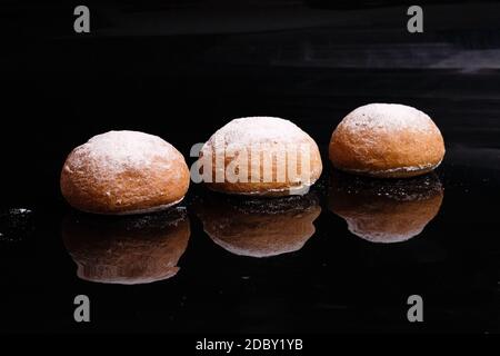 Baking on a black background. White buns sprinkled with powder and flour. Baking at home sprinkled with powder. Stock Photo