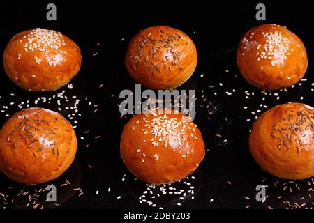 White crispy buns with sesame seeds. Photo on a black background. Homemade pastries are laid out in rows. Stock Photo